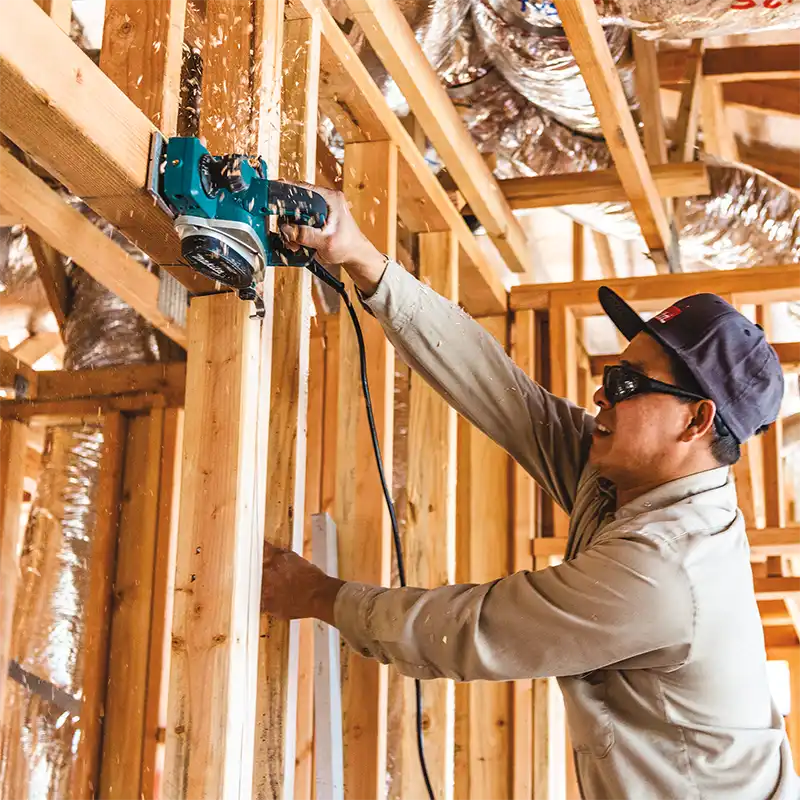 Person using a Makita power tool in a wooden framed building.