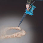 A hand holding a blue and black Makita dust blower, creating a swirl of sand on a dark gray surface.