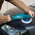 A person using a teal Makita Car Shiner Machine to buff a dark car body in an outdoor setting.