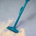 A teal plastic handheld vacuum cleaner head shown on a gray floor, pushing light-colored shreds of paper or wood debris.