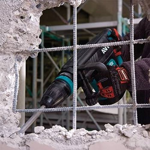 A Makita Concrete Jack Hammer with a metal chisel bit, being operated by a person wearing a black glove on a construction site with concrete rubble and rebar visible.
