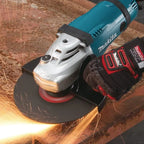 A Makita angle grinder with a black disc attachment actively cutting metal, producing bright sparks. A black and red Makita work glove is worn by the operator, set against a rustic, rusty background.