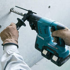 Makita Cordless Rotary Hammer in teal and black colour with white makita being used by a person  