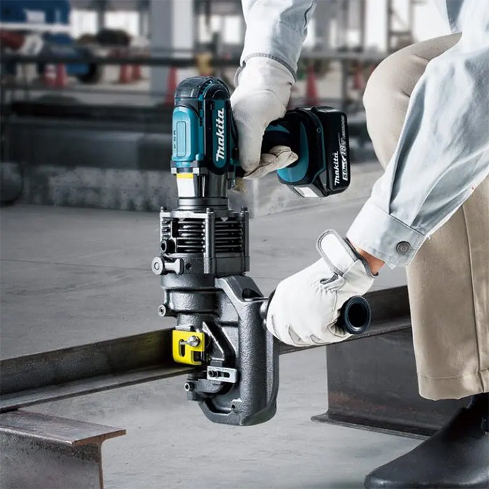 A person wearing white gloves uses a Makite metal hole punch cutter on a steel rail in an industrial setting.