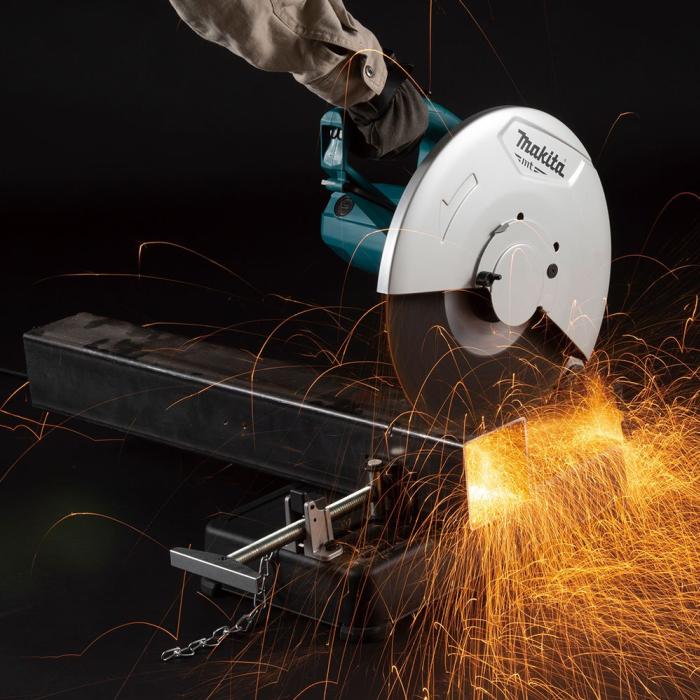 A Makita circular saw with a teal and silver blade is shown cutting a thick metal bar, with bright orange sparks flying against a black background. A person's arm and hand are visible holding the saw.