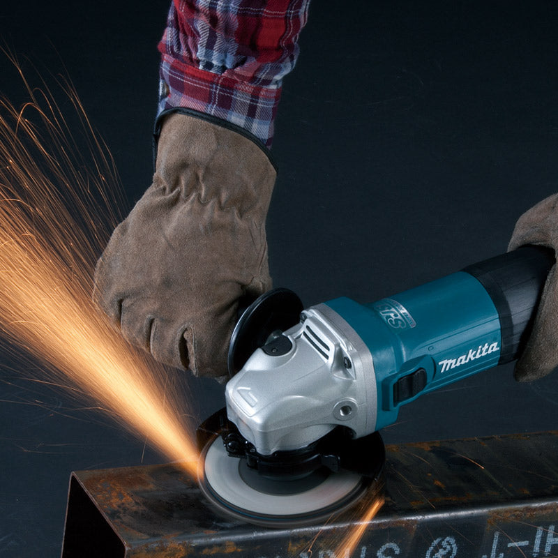 A person wearing a brown leather work glove uses a teal and silver Makita angle grinder to cut metal, with bright orange sparks flying against a dark background.