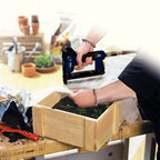 A person using a blue and yellow pneumatic nail gun to fasten a white liner into a wooden raised garden bed on a workbench, with gardening tools and pots in the background.