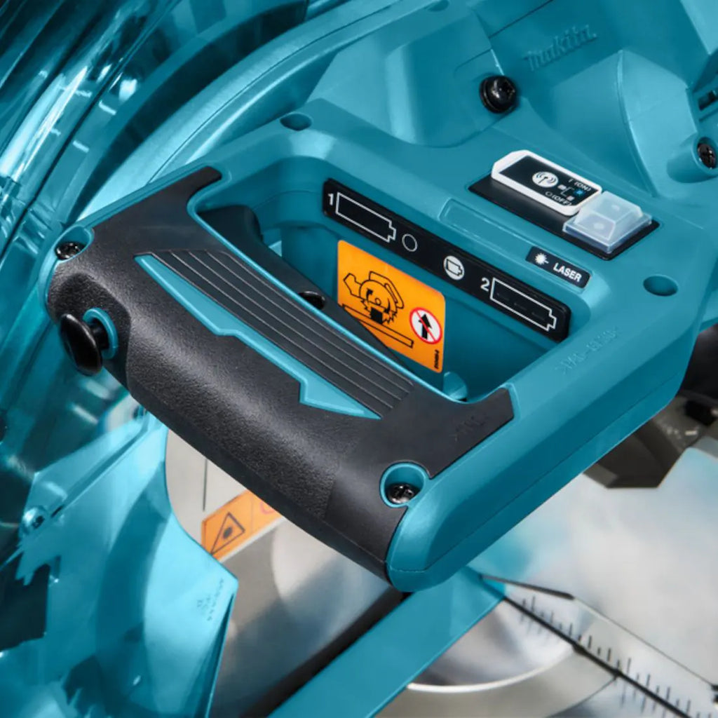 Close-up of a Makita compound miter saw with a teal and black handle, showing the safety switch, laser indicator, and warning labels.