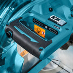 Close-up of a Makita compound miter saw with a teal and black handle, showing the safety switch, laser indicator, and warning labels.