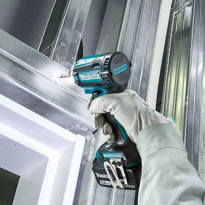 A person wearing a light gray work glove holds a Makita impact driver against a galvanized steel wall or ceiling during installation.