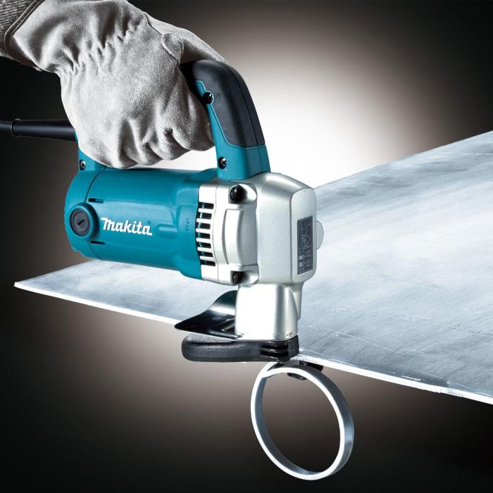 A Makita Metal Shearing Machine, with a metal ring holder, being operated by a gloved hand against a dark studio background.