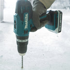 A Makita cordless drill being held by a gloved hand against a light gray concrete floor.