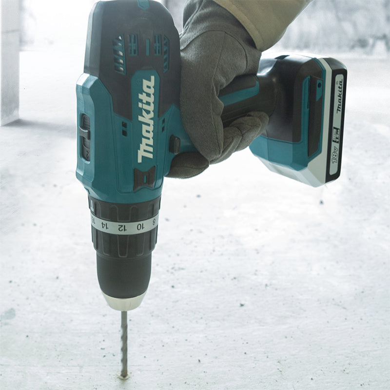 A Makita cordless drill being held by a gloved hand against a light gray concrete floor.