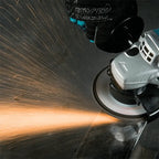 A close-up action shot of a person using a black and teal angle grinder with a circular sanding disc, creating a bright shower of sparks against a dark metal surface. A black glove with the brand name 'FORCE' is visible holding the tool.