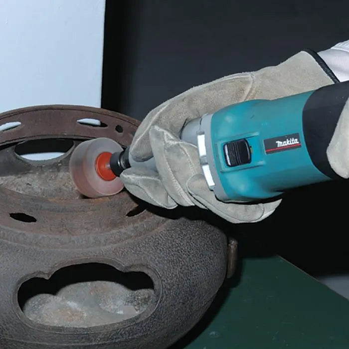 A person wearing a beige leather work glove uses a teal Makita Electric die grinder with a sanding attachment on a cast iron wheel.
