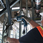 A construction worker wearing safety glasses and gloves uses a blue Makita Makita Dry Wall Screwdriver to fasten metal framing on a construction site.