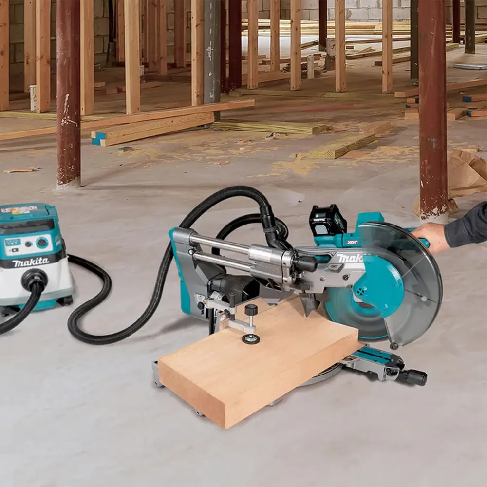 Makita circular saw with a miter gauge and dust collection system in a construction site, cutting a piece of wood. A person's arm is visible on the right side.
